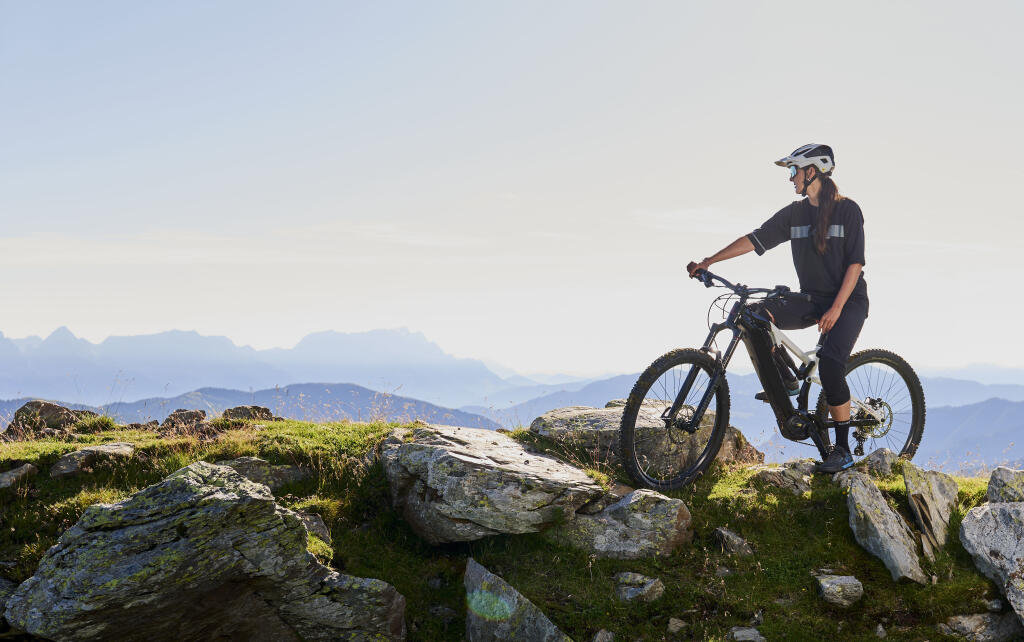 Frau steht mit ihrem Bike auf steinigem Untergrund und schaut in die Ferne