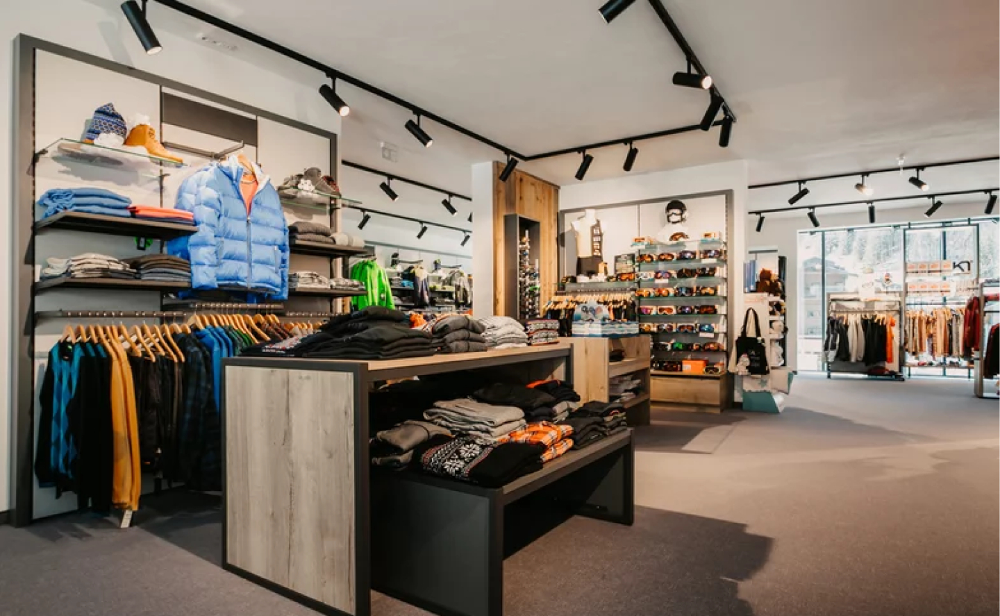 Innenraum eines modernen Bekleidungsgeschäfts mit Kleiderständern und Schienenbeleuchtung.