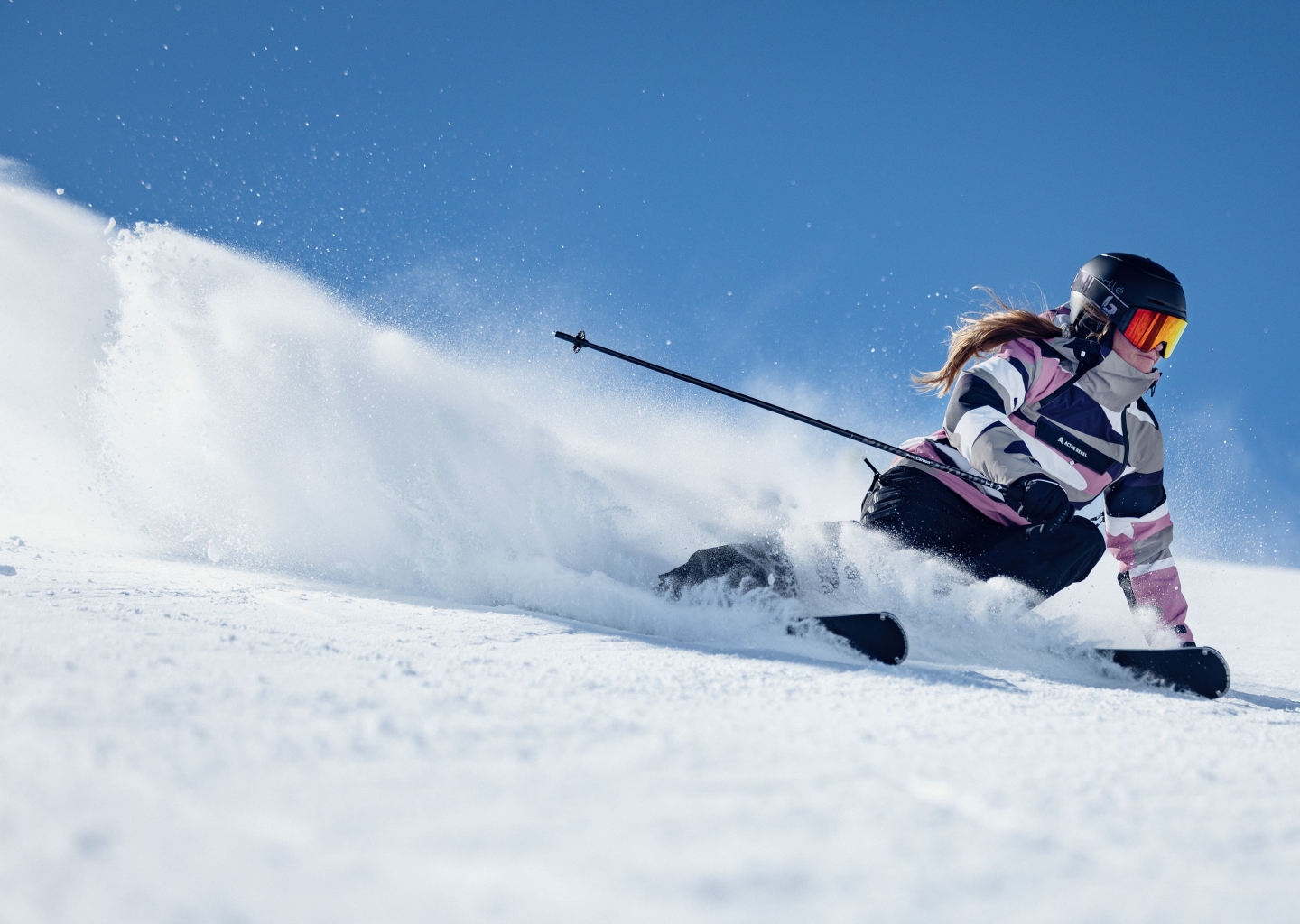 Frau fährt an einem sonnigen Tag Ski einen Hang hinunter und zieht Schwünge durch frischen Pulverschnee.