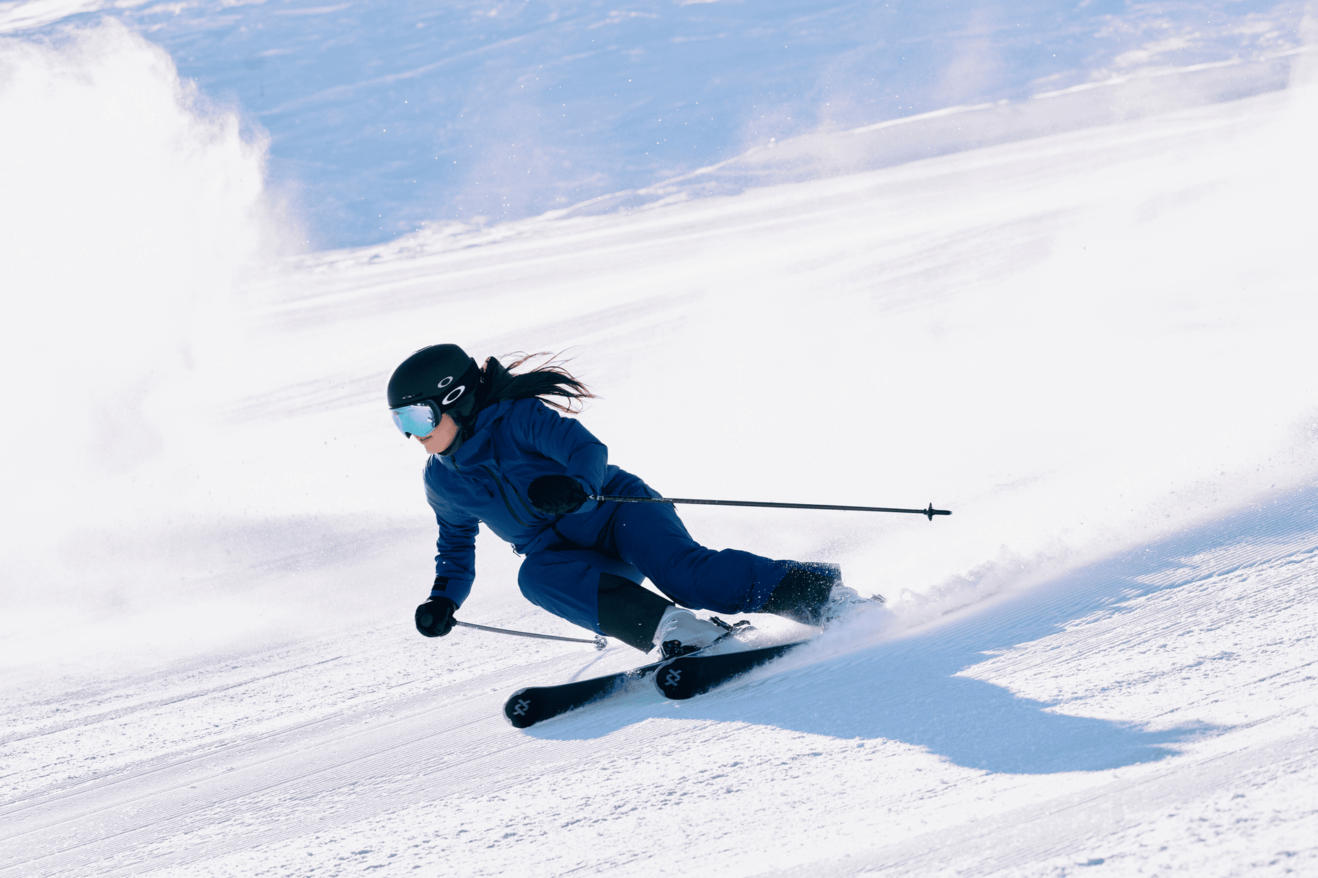 Eine Frau in blauer Skibekleidung fährt die Piste hinunter, hinter ihr eine Schneewolke