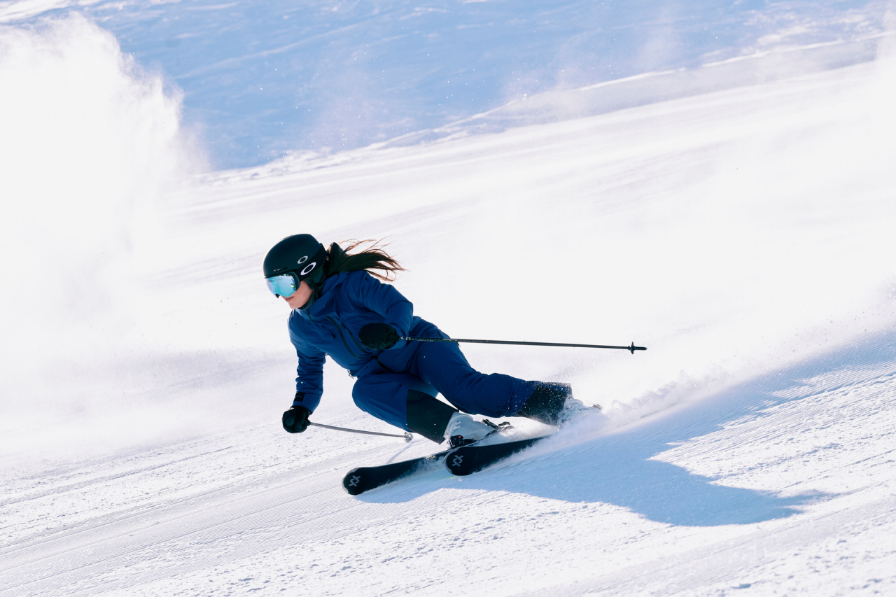 Eine Frau in blauer Skibekleidung fährt die Piste hinunter, hinter ihr eine Schneewolke