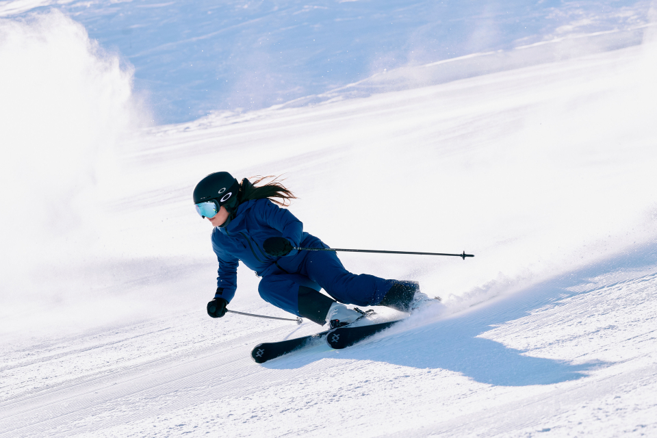 A woman in blue ski clothing is skiing down the slope, leaving a cloud of snow behind her.