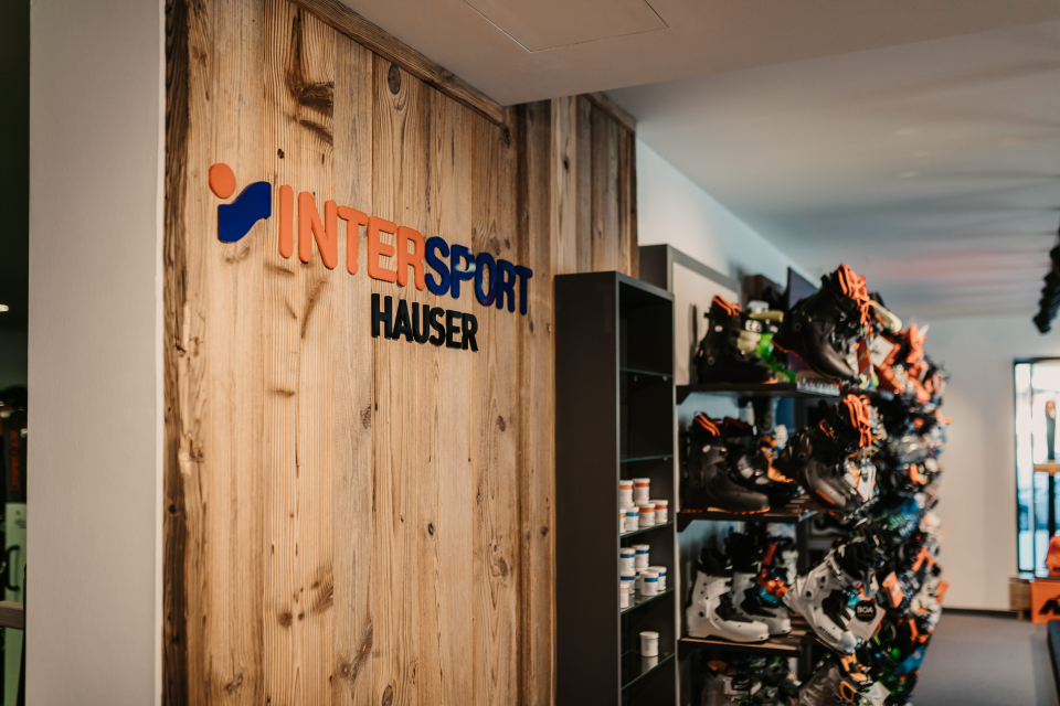 INTERSPORT Hauser Logo auf einer Holzwand, rechts daneben Regale